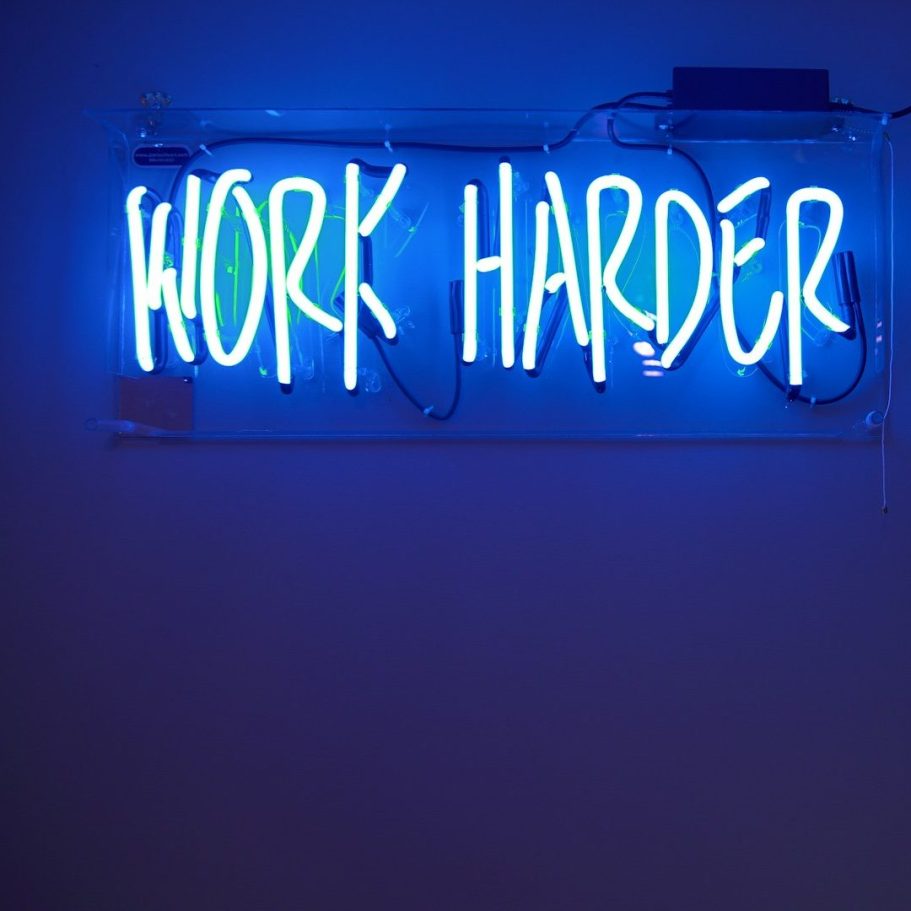 Neonleuchtschrift „WORK HARDER“ in blauem Licht.