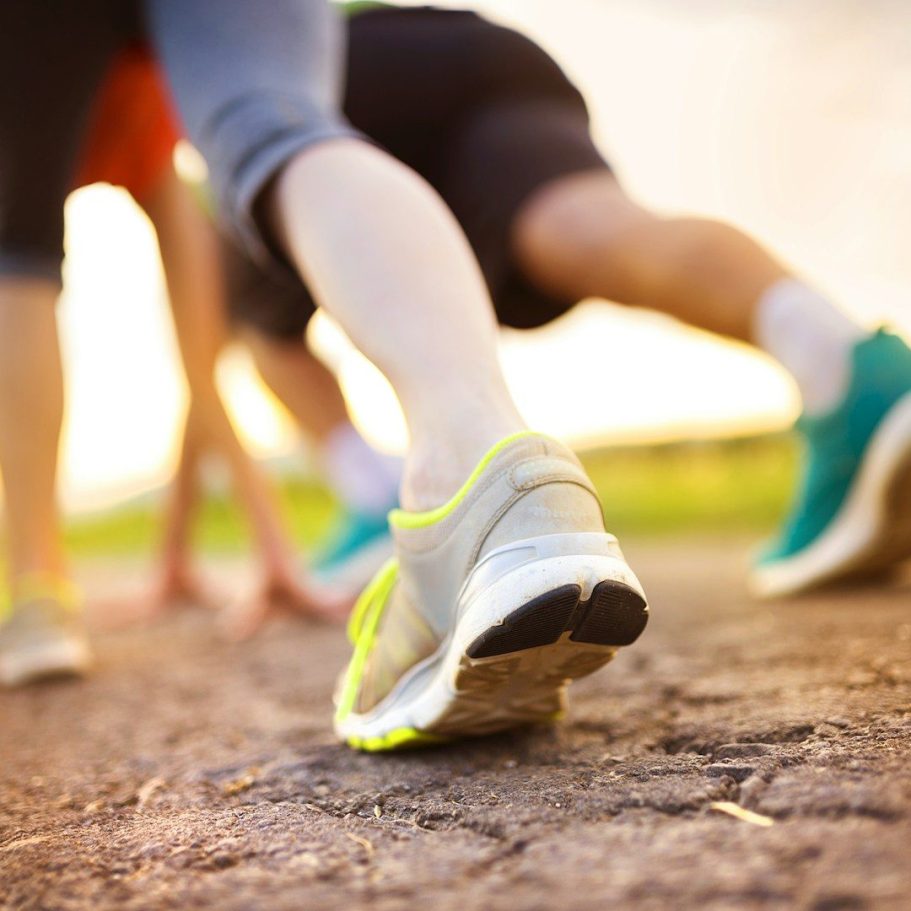Füße in Laufschuhen und Hände in Startposition auf auf einem Sportplatz.