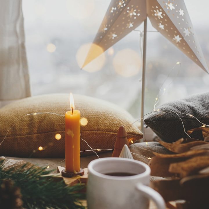 Gemütliche Winterdekoration mit Kerze, Kaffeetasse und Sternenlaterne auf einem Tisch.