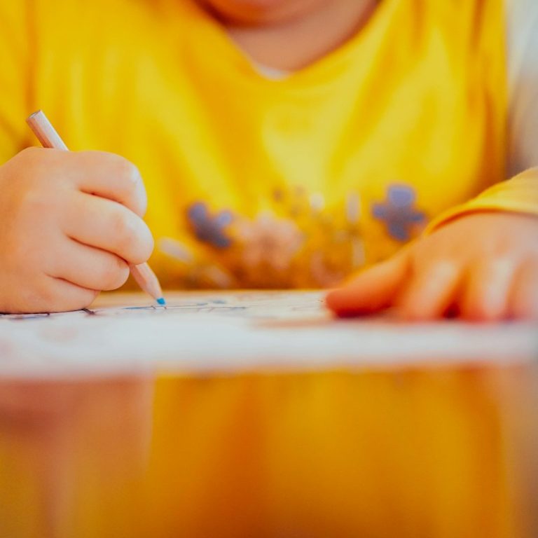 Schreibendes Kind Ein Kind schreibt mit Stift auf einem Blatt Papier.