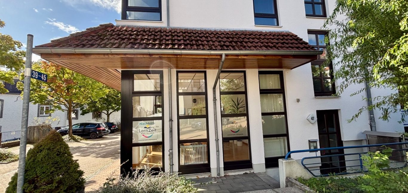 Eingang zu einem modernen Gebäude mit großzügigen Fenstern und einem Vordach.