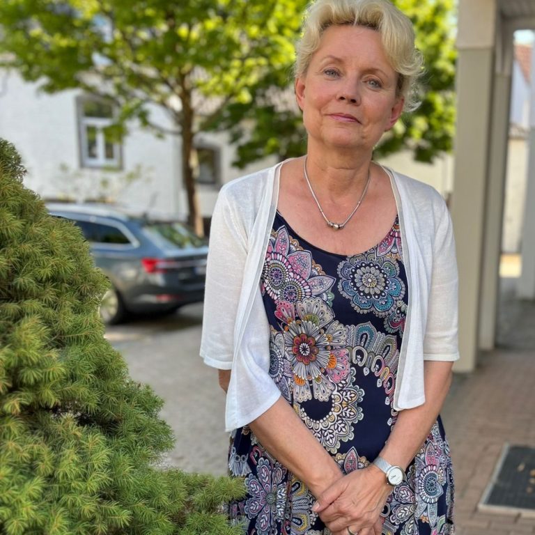 Frau mit blonden Haaren in floralem Kleid steht vor draußen vor Nachhilfeschule.