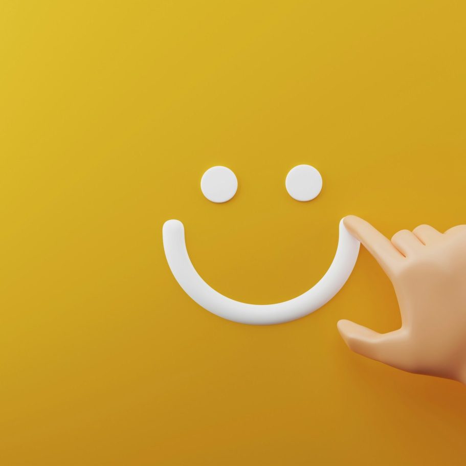Hand zeichnet weißen Smiley auf gelbem Hintergrund.