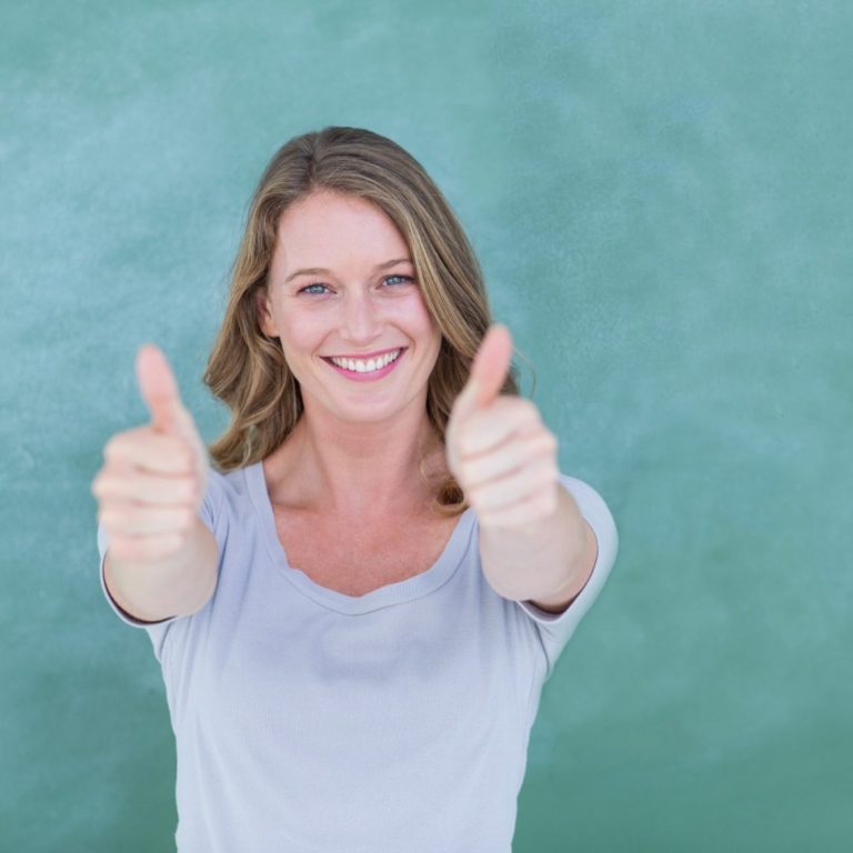 Lächelnde Frau, eine Lehrerin, steht mit Daumen nach oben vor einer grünen Tafel