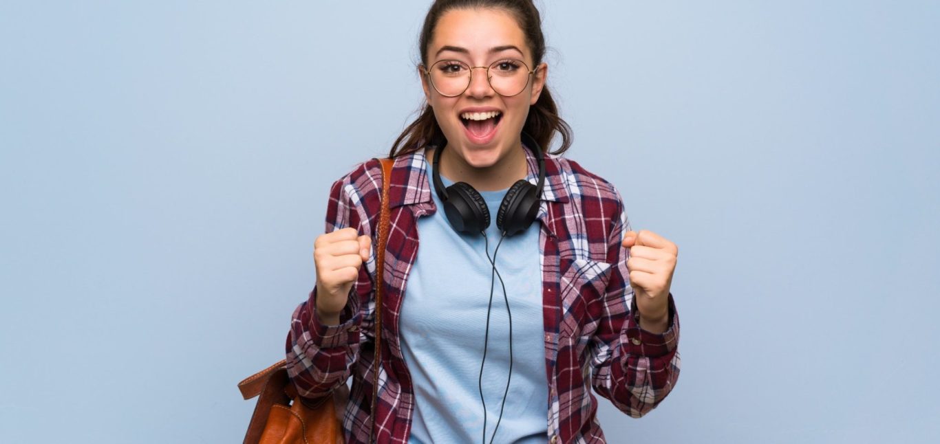 Junge Frau mit Kopfhörern, lächelnd und mit erhobenen starken Fäusten, trägt eine Umhängetasche.